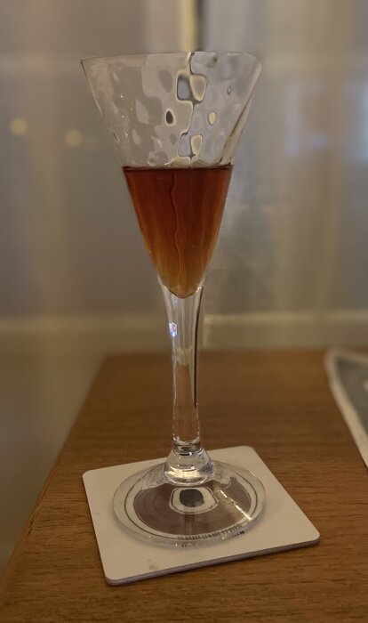 Ett glas med mörk vätska på en bordsunderlägg mot suddig bakgrund.