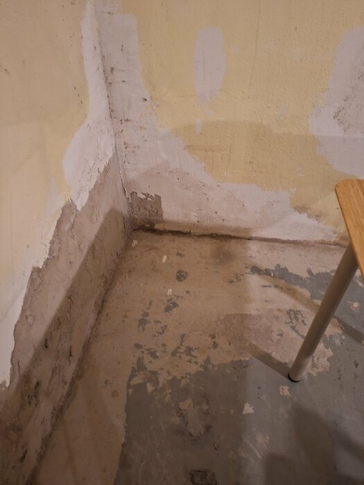 Ett hörn av ett tomt rum under renovering med flagnande väggfärg och ojämnt betonggolv.