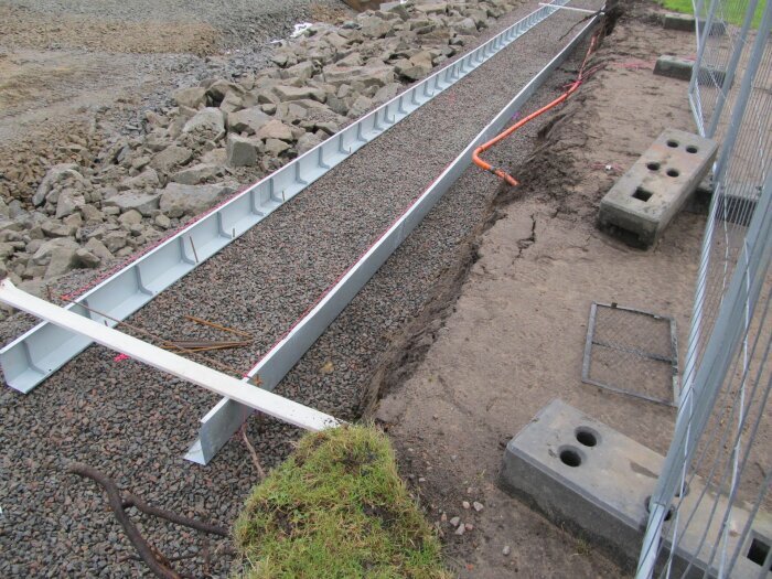 Grundkonstruktion med grus, stålspont, byggnadsställning, grävd mark, säkerhetsstaket under förberedande konstruktionsarbete.