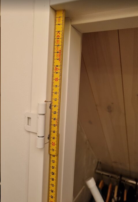 Mätsticka vertikalt mot dörrkarm, mäter dörröppning, förmodligen för hemmaprojekt eller -renovering.