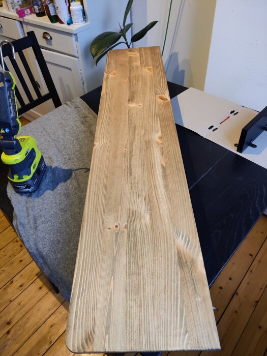 Träbräda på bord nära borr, inomhus, DIY-projekt, bordsskiva som förbereds eller renoveras, verktyg och växt synliga.