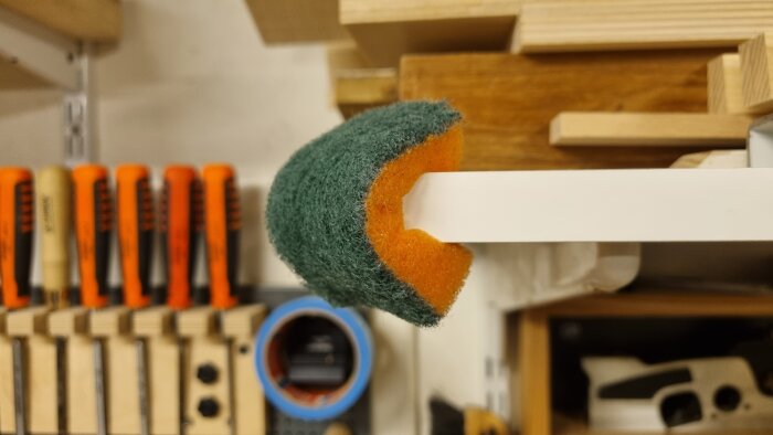 Grön och orange svamp på vit hylla, verktyg och trä i bakgrunden, närbild, inomhusmiljö, arbetsrum, lutande perspektiv.