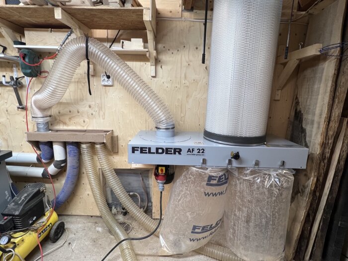 Verkstadsdammutsug med filter och två uppsamlingspåsar, märkt "FELDER AF 22", träsvarv, hyllor, kabeldragning.