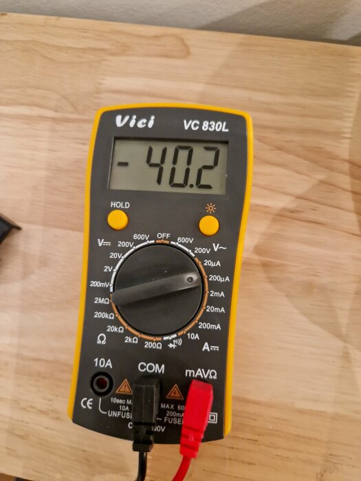 Multimeter på träyta visar -40.2 grader Celsius, troligen temperaturmätning, röda och svarta ledningar anslutna.