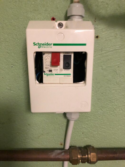 Schneider Electric elektricitetscentral med röd stoppknapp och grön startknapp på en målad vägg.