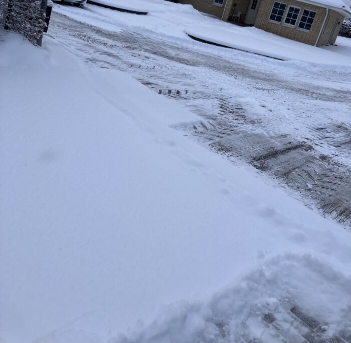 Snötäckt område med hus, snöspår, kallt väder, oplogad yta framför byggnad.