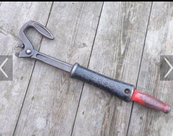 Gammal kofot ligger på trägolv, verktyg med röd-svart handtag och sliten metal.
