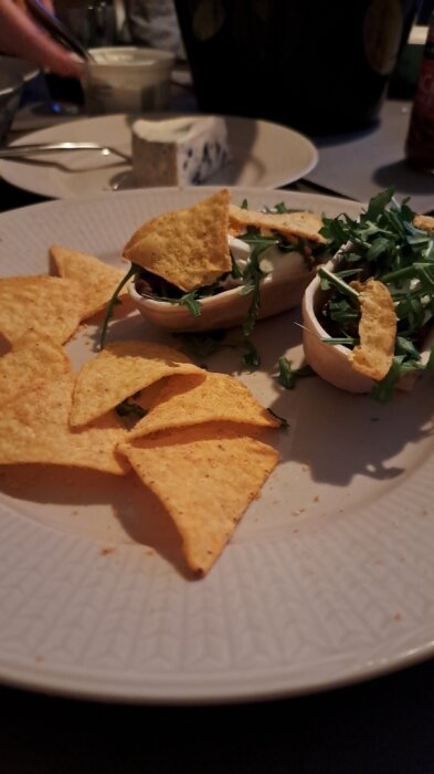 Tortillachips med en fylld maträtt och gröna örter på ett vitt fat.