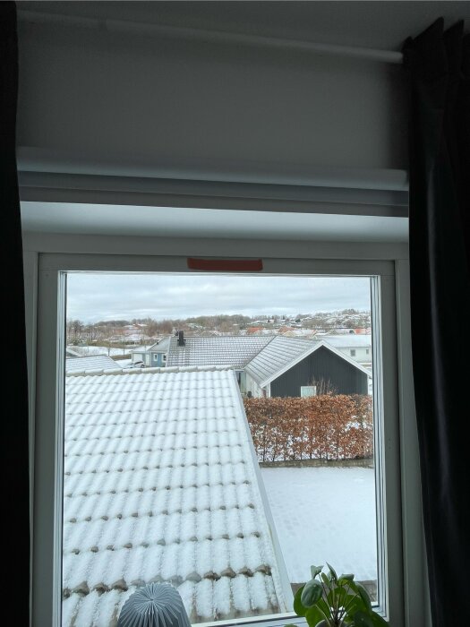 Ett fönster med utsikt över snötäckta hustak och en grå himmel.