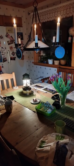 Mysig, hemtrevlig köksinteriör med tända ljus, blommor, papperspynt och ett rörigt matbord.