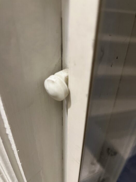Vit dörrstopp i plast på en sliten, vitmålad dörrkarm i en interiör miljö.