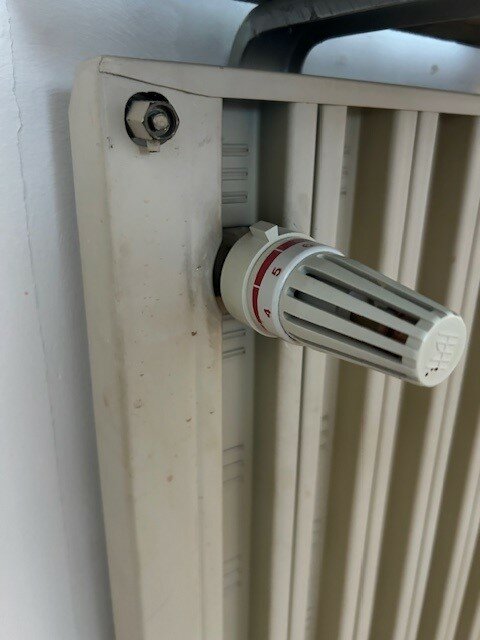 Termostatventil på en vit radiator, smutsfläckar, används för att justera värmen.