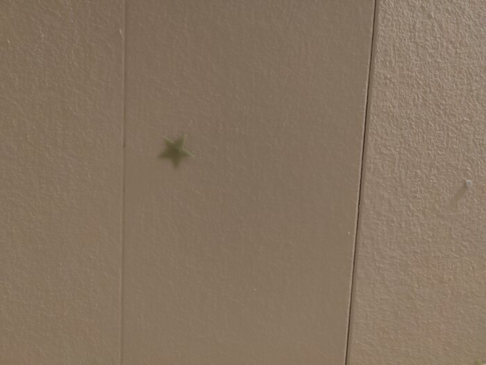 En grön stjärnformad klistermärke på en beige vägg med texturlinjer.