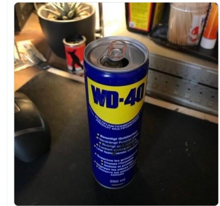WD-40-burk förklädd som dryckesburk. Arbetsbänk bakgrund. Humoristisk bild, oväntad design.