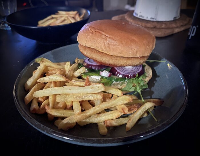 Hamburgare med lök, sallad på tallrik, friterade pommes frites, mörk bakgrund.