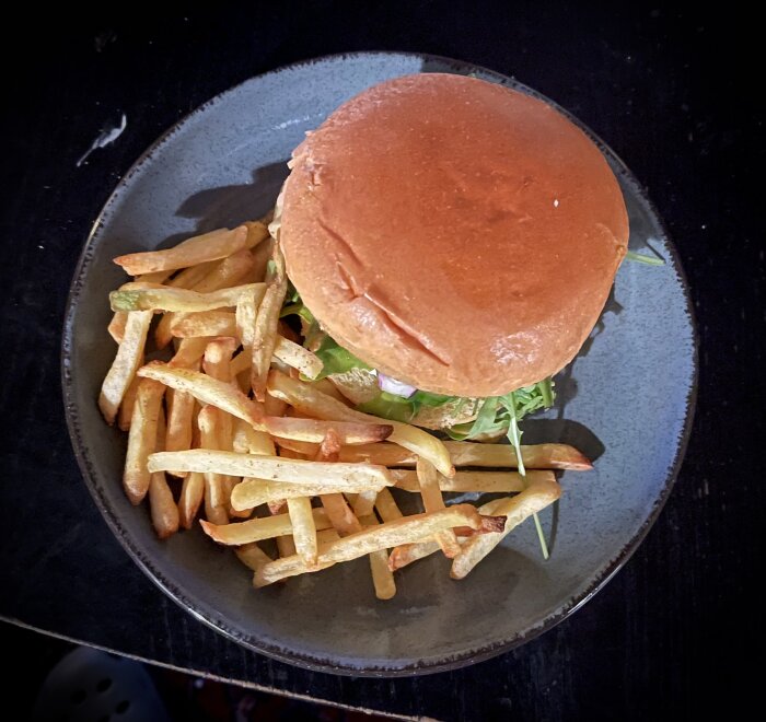 En hamburgare med sallad på en tallrik bredvid en hög pommes frites.