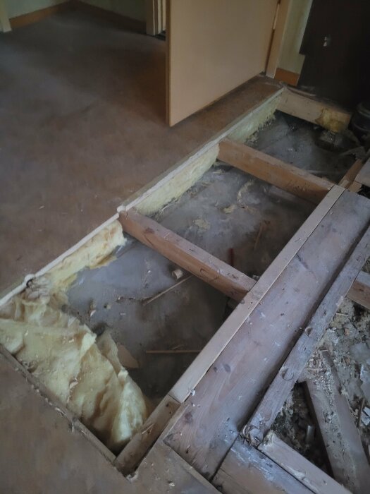Öppet golv med synlig isolering och träreglar i ett gammalt rum under renovering.