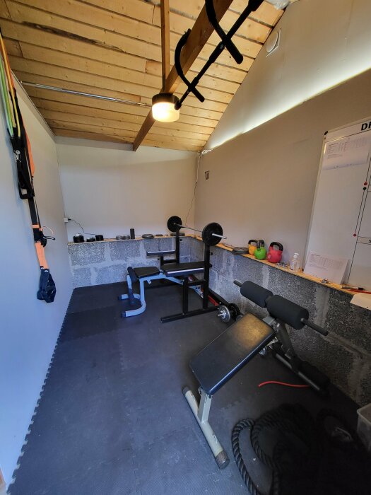 Garage omvandlat till gym med styrketräningsutrustning, mattor, vikter och vit anslagstavla.