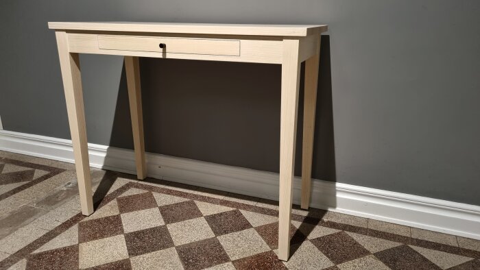 Träkonsolbord, en låda, mörkgrå vägg, rutigt golv, vit golvlister, minimalistisk design.