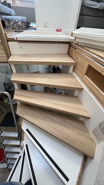 Trappa under konstruktion, trästeg, verktygslåda och byggmaterial synliga, oavslutat projekt, inomhusmiljö, spegelbild av person.