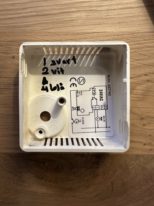 En plastlåda med anteckningar och ett elektriskt schema, mot träbakgrund.