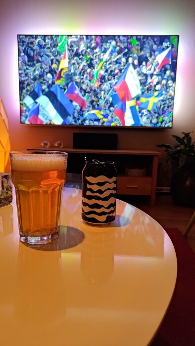 Ett vardagsrum med ett öppet öl, ett glas och fotbollsmatch på TV:n.