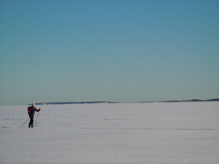 En person skidar över ett snötäckt, fruset landskap under en klarblå himmel.