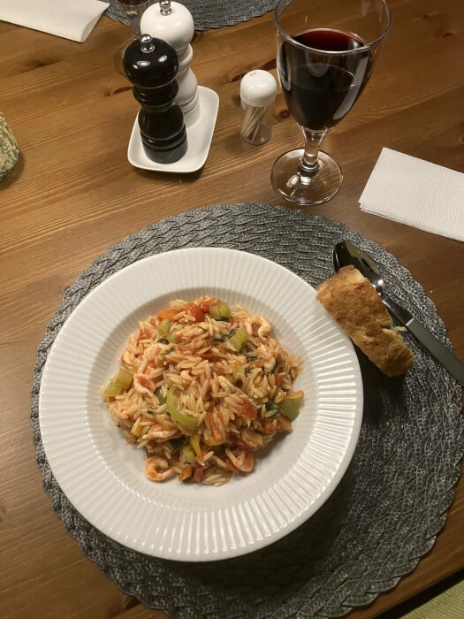 Middagstillfälle med pasta, vin, salt- och pepparkvarnar samt brödbit på bord.