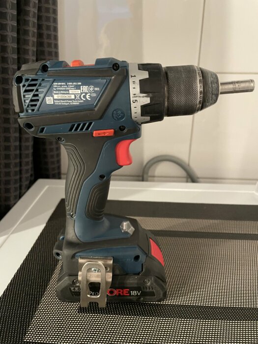 En blå och röd sladdlös borrskruvdragare med batteri, placerad på ruvad yta.