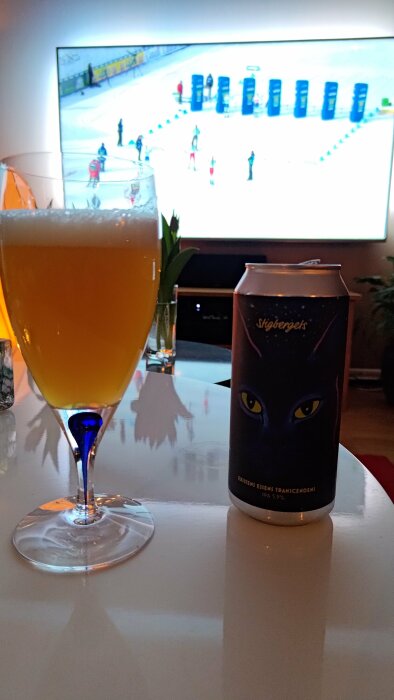 Ett glas öl, en burk, TV med sport, mysig hemmiljö.