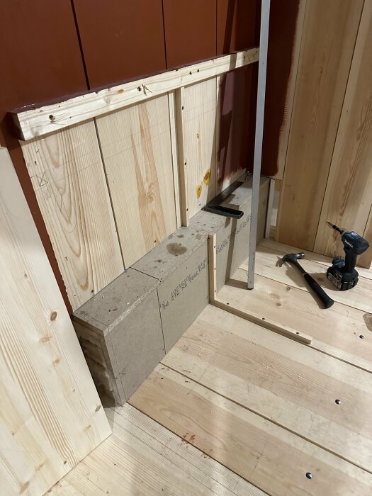 Byggarbetsplats med träpaneler, betongblock, och konstruktionsverktyg på ett trägolv i inomhusmiljö.