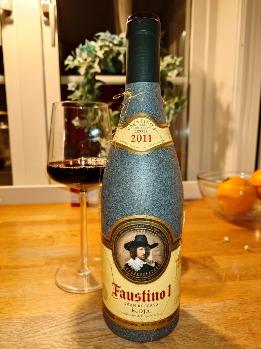 Flaska av Faustino I Rioja Gran Reserva 2011 vin, närbild, fyllt vinglas i bakgrunden, köksmiljö.