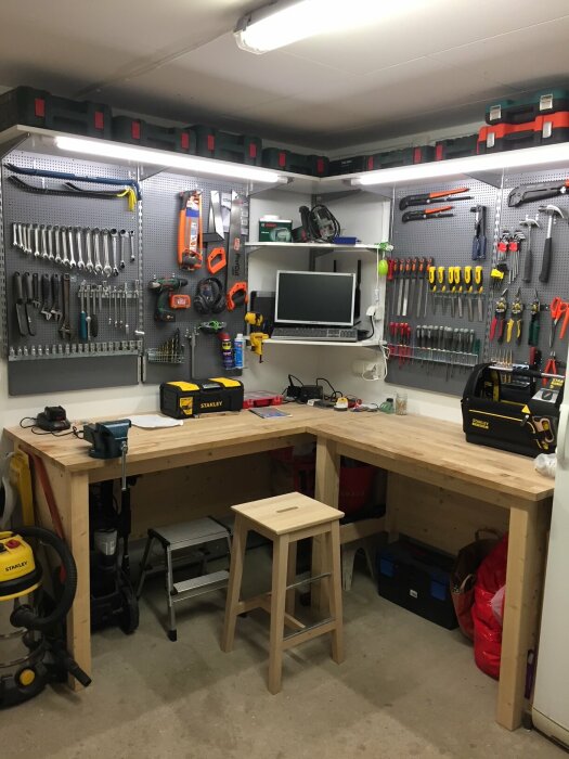 Välordnat garage med arbetsbänk, verktyg på väggskivor, och belysning.