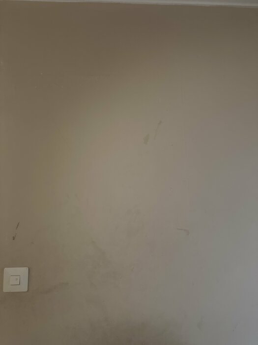 En vägg med fuktfläckar och en eluttag. Behov av renovering eller målning syns.