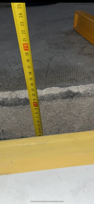 Måttband mäter höjd på gult vägblock, detaljerad markyta och mätparametrar synliga.