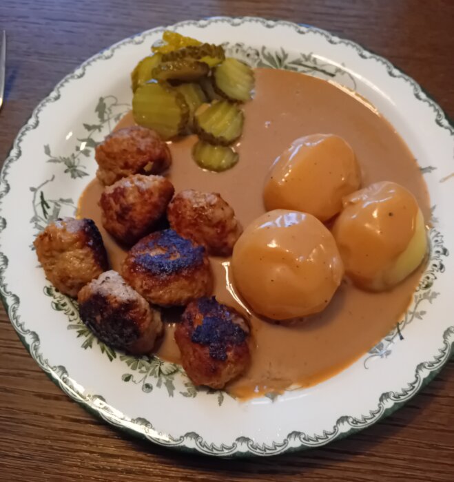 Köttbullar, potatis, brunsås, inlagda gurkor på dekorerad tallrik, traditionell mat, hemlagat, middag.