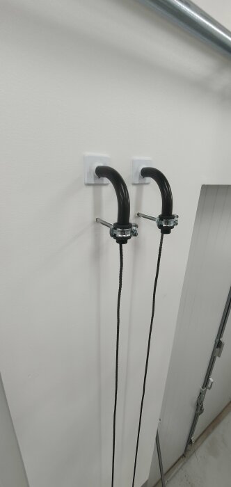 Två svarta kablar hänger från väggmonterade krokar nära en trappa, liknar frågande ansikten.