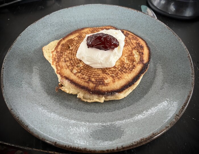 Amerikansk pannkaka med grädde och sylt på en blå tallrik.