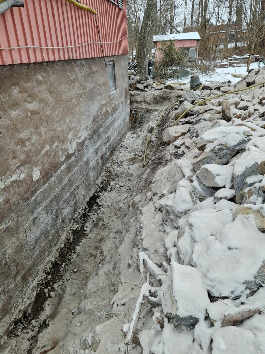 Grund av hus, snöbelagda stenar, utgrävningsarbete, kallt väder, ojämn terräng, bar mark.