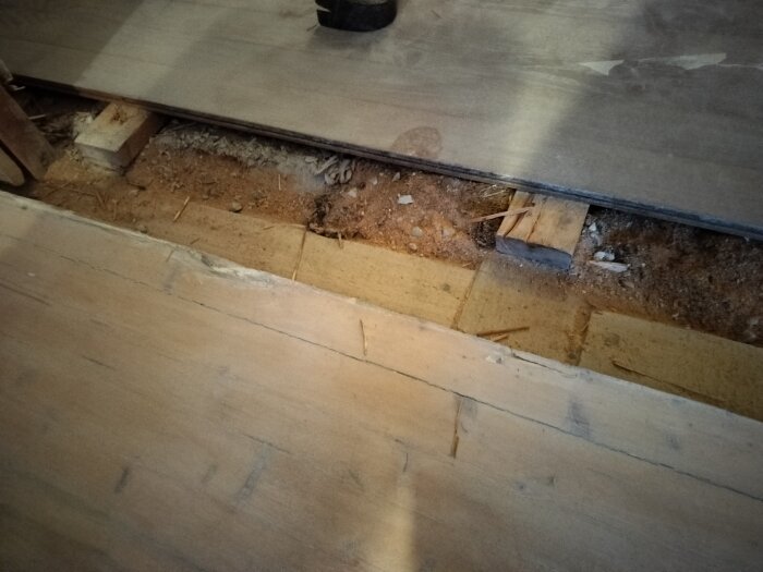Reparation eller installation av golv, oskyddade golvbjälkar och isolering, byggnadsarbete pågår.