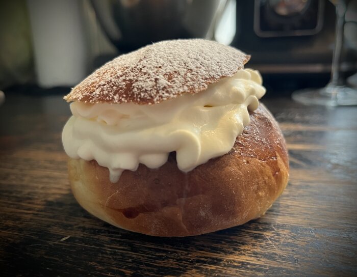 Semla med fluffigt grädde och pudrat florsocker på ovansidan. Traditionellt svenskt fettisdagsbakverk på träbord.