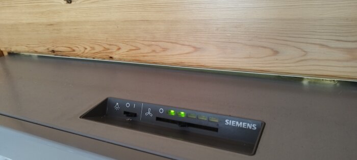 Kontrollpanelen på en diskmaskin från Siemens integrerad under en träarbetsyta; gröna lampor och symboler syns.