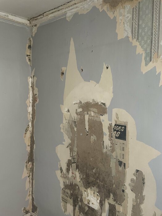 Hörnrum med slitet och fuktigt tapet, flagnande och avskalad vägg, renoveringsbehov synligt.