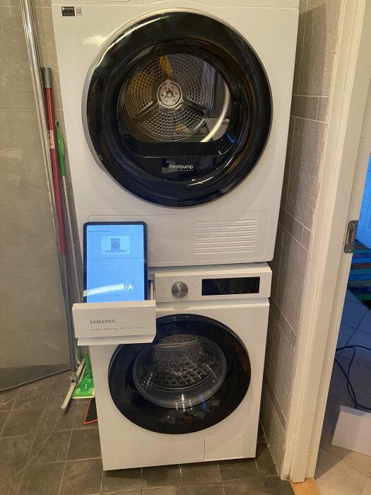 Staplad tvättmaskin och torktumlare i ett tvättrum med Samsung-skylt och grön mopp.