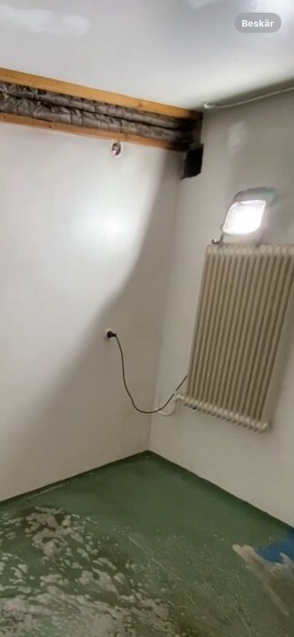 Ett rum under renovering, kalt, kablar dinglar, radiator, ofärdigt golv, tomhet.