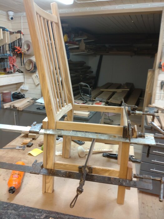En snickarverkstad med verktyg, trästycken och en pågående stolskonstruktion fastspänd med tvingar.