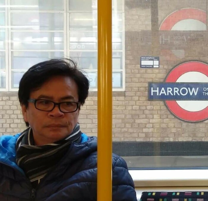 Person sitter inne i ett tåg; Harrow on the Hill tunnelbanestation syns utanför fönstret.