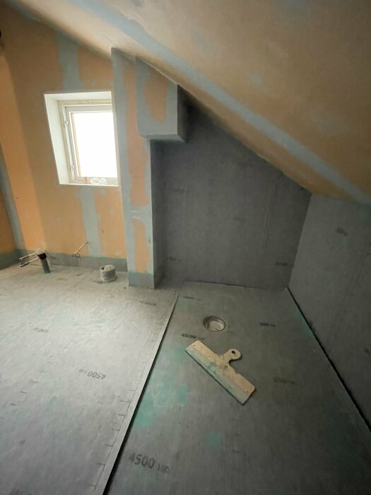 Renoveringsarbete i ett snedtakat rum med isolering och gipsskivor. Verktyg och material på golvet.