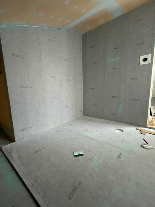 Ett rum under renovering med isoleringsskivor på väggarna och skyddspapp på golvet.