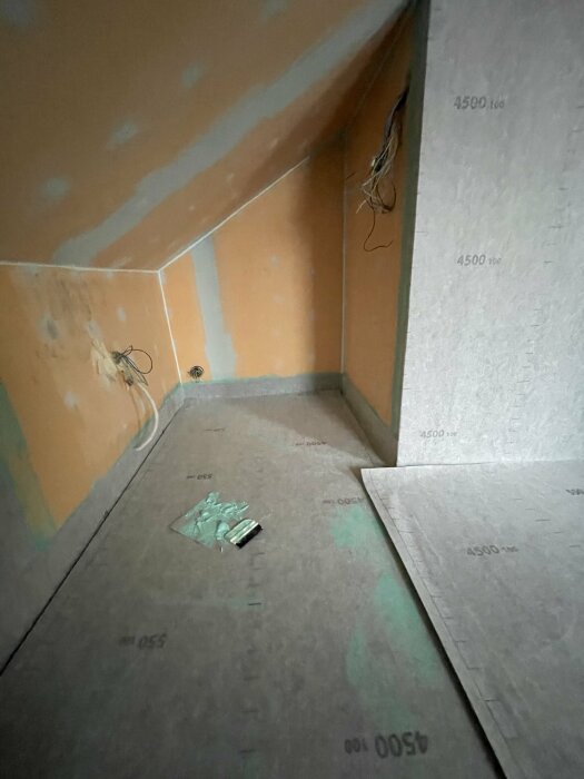 Ett ofärdigt rum med isoleringsplattor på golvet och uttagna hål för elinstallationer i väggarna.